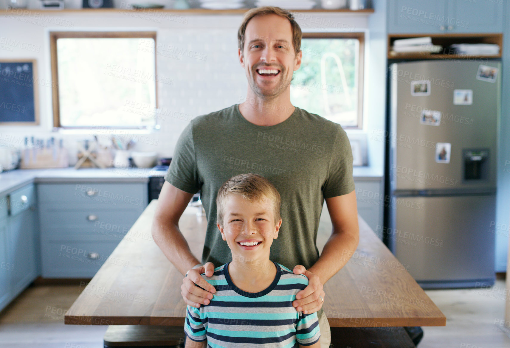 Buy stock photo Cropped portrait of an affectionate young father looking cheerful while standing with his son in their kitchen at home