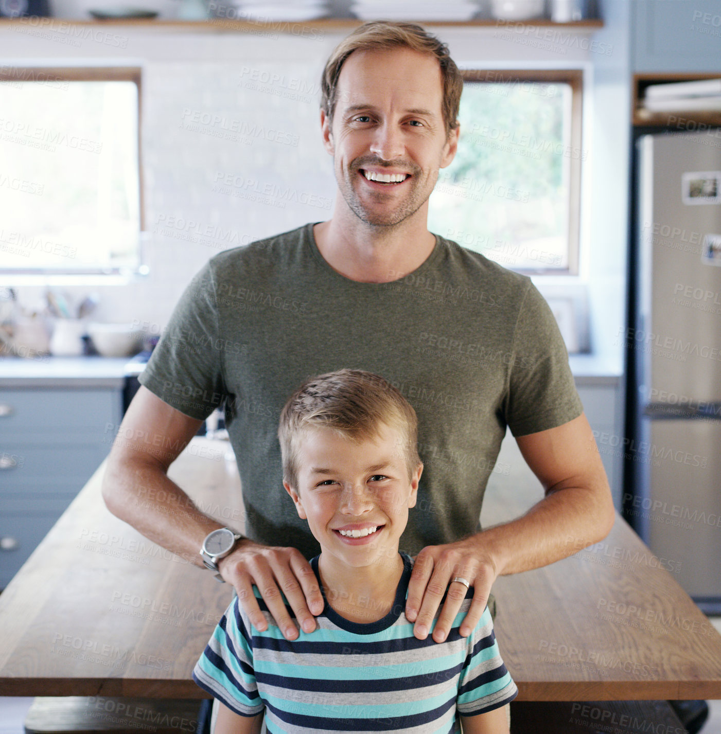 Buy stock photo Cropped portrait of an affectionate young father looking cheerful while standing with his son in their kitchen at home