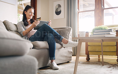 Buy stock photo Full length shot of an attractive young woman looking cheerful while shopping online using a digital tablet at home