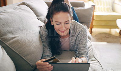 Buy stock photo Cropped shot of an attractive young woman using a digital tablet and a credit card to shop online while lying on a couch at home