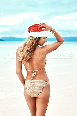 Buy stock photo Shot of a young woman wearing a christmas cap while standing on the beach