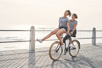 Buy stock photo Shot of two friends having fun cycling along the coastline