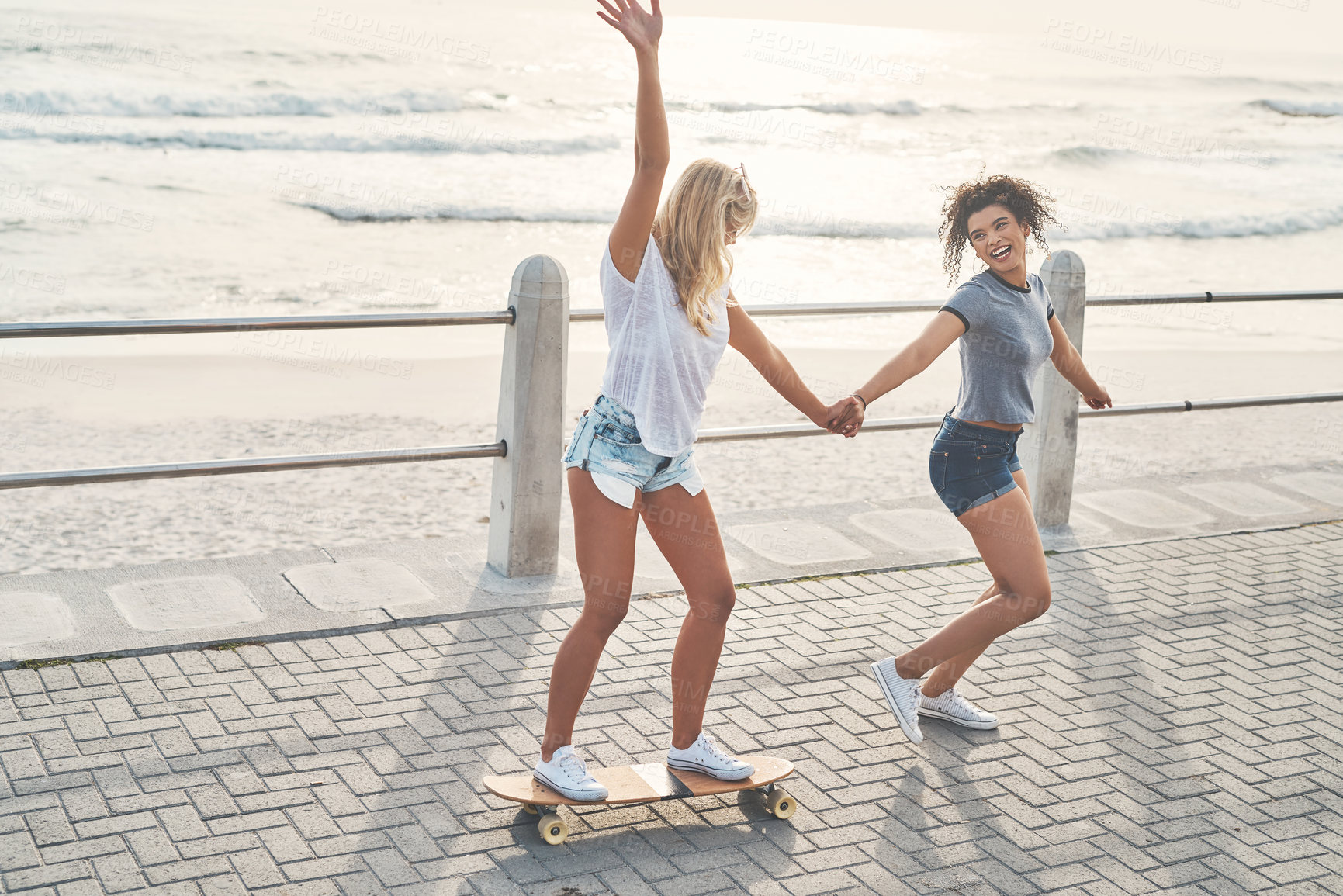 Buy stock photo Beach, women and friends with skateboard, holding hands and summer holiday with fun, playful and smile. People, seaside and outdoor with happiness, girls and skating with sunshine, joyful or carefree