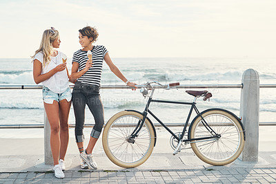 Buy stock photo Shot of two friends eating ice cream while standing on the promenade with a bicycle