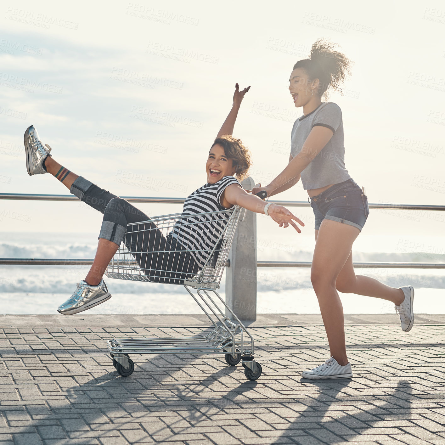 Buy stock photo Friends, girls and fun with trolley outdoor for freedom, bonding and transport ride of beach travel in summer. People, women and smile with shopping cart for play activity, relax and ocean together