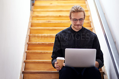 Buy stock photo Cropped shot of a handsome young businessman sitting alone on the staircase alone and using his laptop