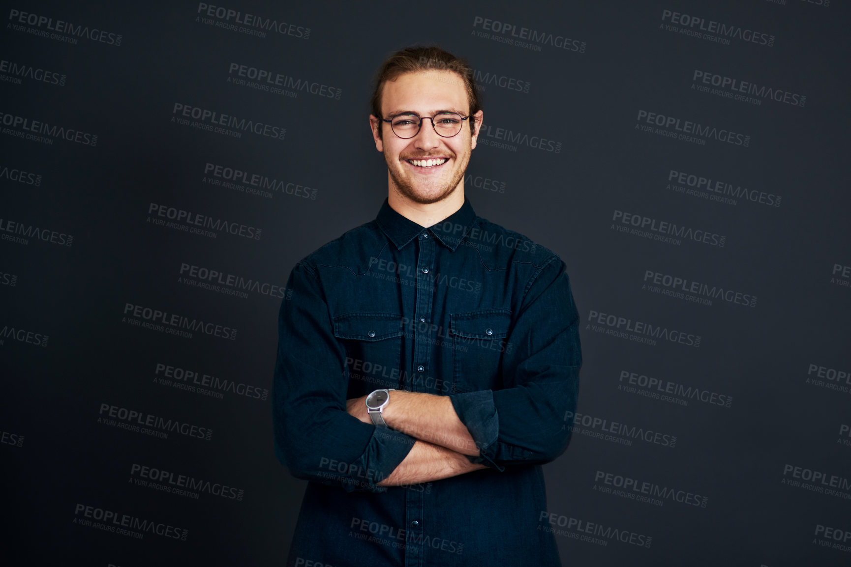 Buy stock photo Cropped portrait of a handsome young businessman standing alone with his arms folded against a black background in the studio