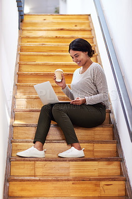Buy stock photo Full length shot of an attractive young businesswoman sitting on a wooden staircase and using her laptop while holding coffee