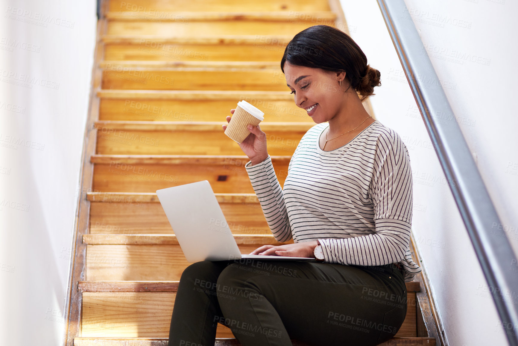 Buy stock photo Cropped shot of an attractive young businesswoman sitting on a wooden staircase and using her laptop while holding coffee