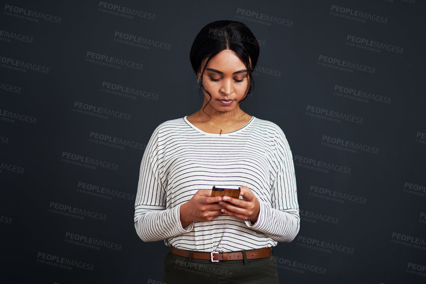 Buy stock photo Cropped shot of an attractive young businesswoman standing alone and texting on her cellphone against a black studio background