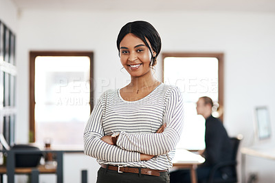 Buy stock photo Cropped portrait of an attractive young businesswoman standing with her arms folded while her colleague works behind her