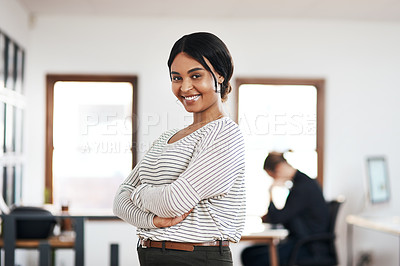 Buy stock photo Cropped portrait of an attractive young businesswoman standing with her arms folded while her colleague works behind her