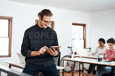 Buy stock photo Cropped shot of a handsome young businessman using a tablet while his colleagues work behind him in the office