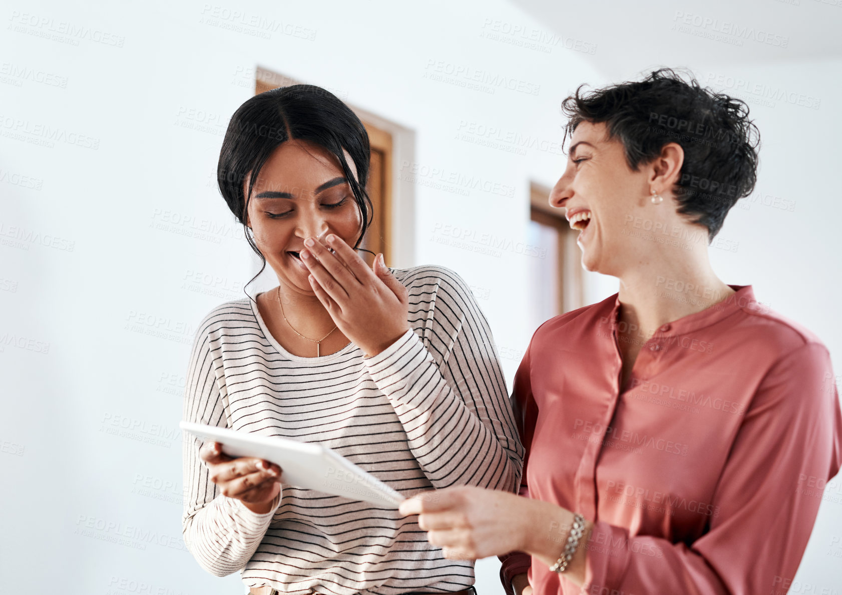 Buy stock photo Cropped shot of two attractive young businesswomen standing together in the office and laughing while using a tablet
