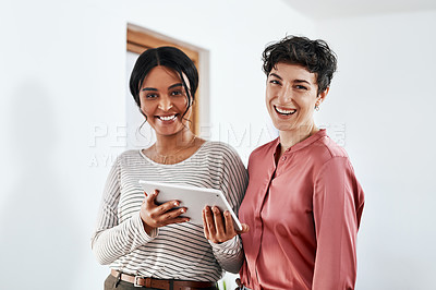 Buy stock photo Cropped portrait of two attractive young businesswomen standing together in the office and using a tablet
