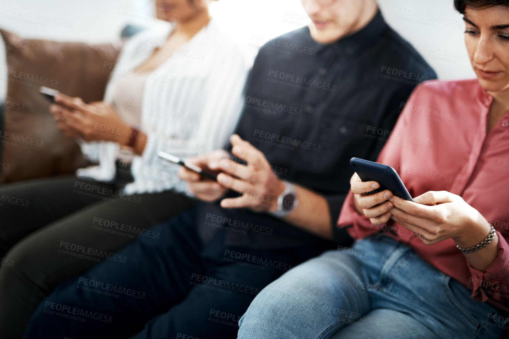 Buy stock photo Cropped shot of a diverse group of businesspeople sitting in the office together and texting on their cellphones