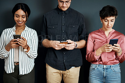 Buy stock photo Cropped shot of a diverse group of businesspeople standing against a gray background and texting on their cellphones