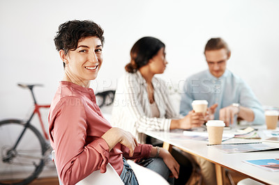 Buy stock photo Cropped portrait of an attractive young businesswoman sitting and smiling while her colleagues have a meeting behind her