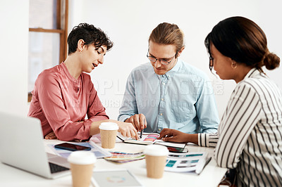 Buy stock photo Cropped shot of a diverse group of businesspeople sitting together and reading paperwork during a meeting in the office