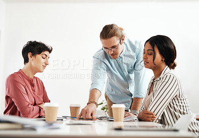 Buy stock photo Cropped shot of a diverse group of businesspeople sitting together and reading paperwork during a meeting in the office