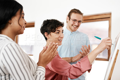 Buy stock photo Cropped shot of an attractive young businesswoman standing and writing on a white board while her colleagues clap for her