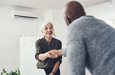 Buy stock photo Cropped shot of two cheerful businesspeople shaking hands in agreement inside of the office during the day