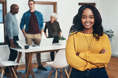 Buy stock photo Portrait of a cheerful young businesswoman standing with her arms folded and her work colleagues in the background inside of the office