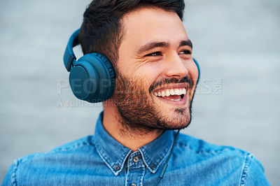 Buy stock photo Cropped shot of a handsome young man smiling while listening to music on his headphones against a brick wall