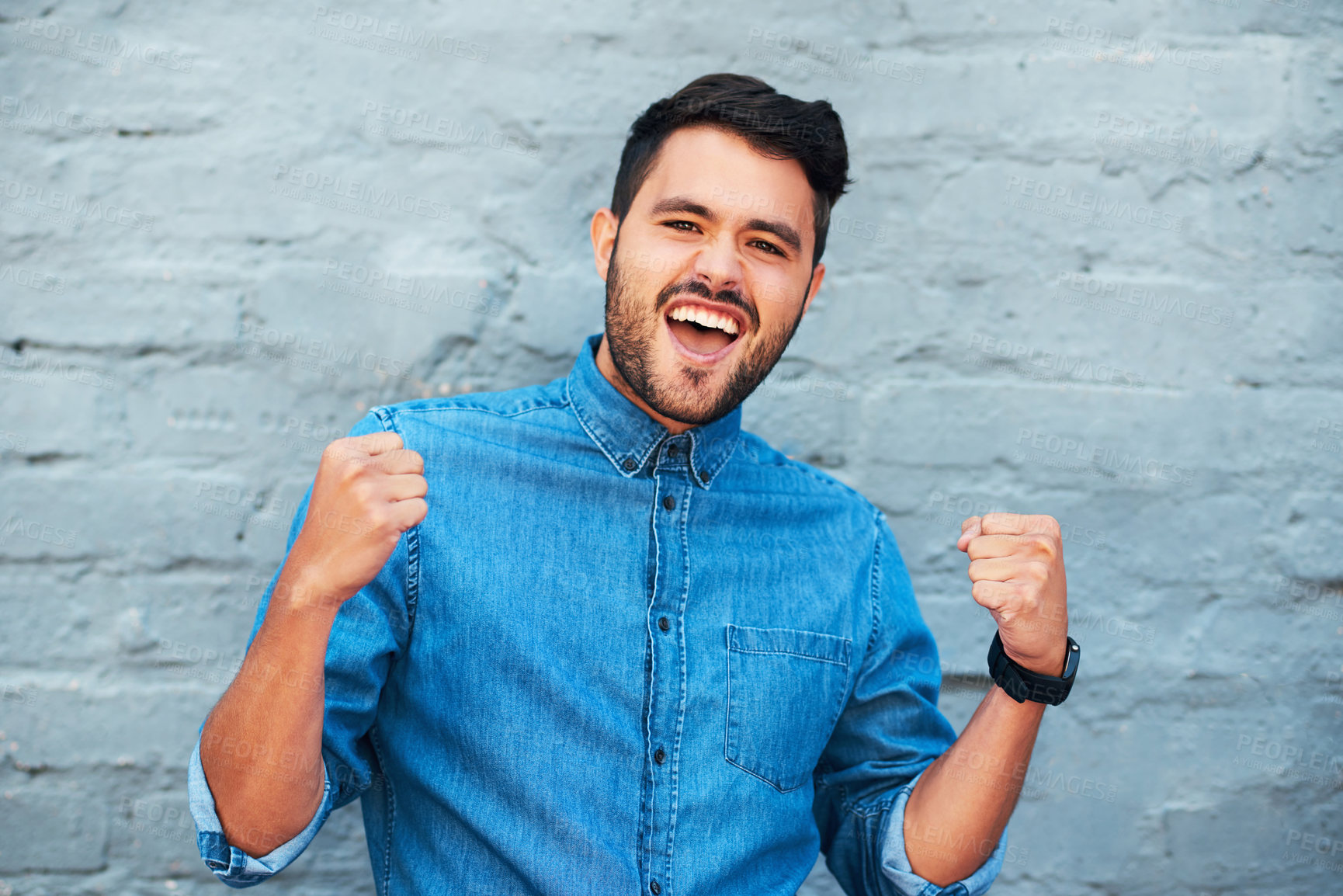 Buy stock photo Cropped portrait of a handsome young man cheering while standing against a brick wall