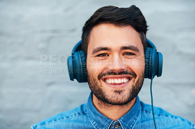 Buy stock photo Cropped shot of a handsome young man smiling while listening to music on his headphones against a brick wall