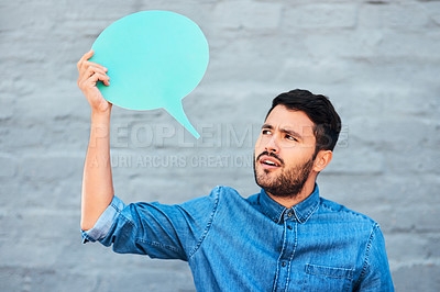 Buy stock photo Cropped shot of a handsome young man looking skeptical while holding a speech bubble against a brick wall