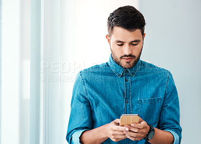 Buy stock photo Cropped shot of a handsome young businessman using a mobile phone while standing in an office