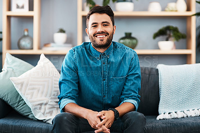 Buy stock photo Cropped portrait of a handsome young man smiling while sitting on a couch in his living room at home