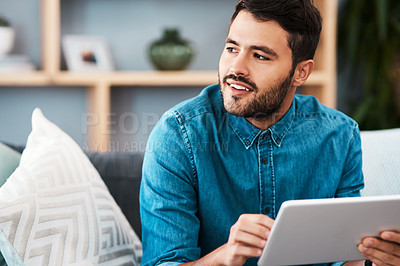 Buy stock photo Cropped shot of a handsome young man looking thoughtful while using a digital tablet in his living room at home