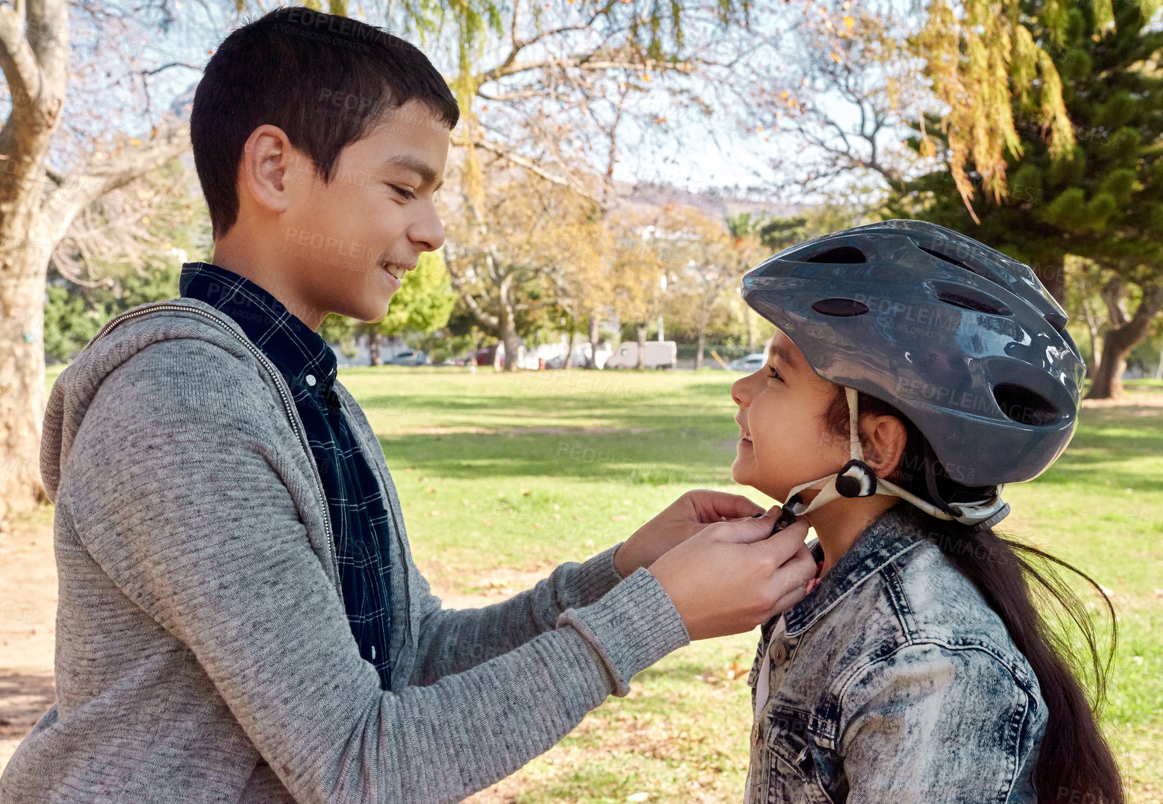 Buy stock photo Shot of a young boy helping to secure his sister’s helmet before she rides her bicycle in the park