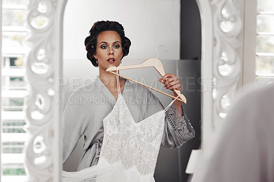 Buy stock photo Cropped shot of a woman holding her wedding dress against her while looking in the mirror