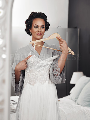 Buy stock photo Cropped shot of a woman holding her wedding dress against her while looking in the mirror