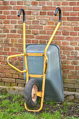 Buy stock photo Garden wheelbarrow leaning against a red brick wall in a home backyard. Landscaping equipment and tools to carry and transport soil, manure, compost and fertilizer. Done cleaning a landscaped yard