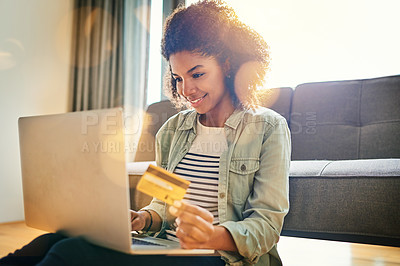 Buy stock photo Shot of a cheerful young woman doing online shopping on her laptop while being seated on the floor at home
