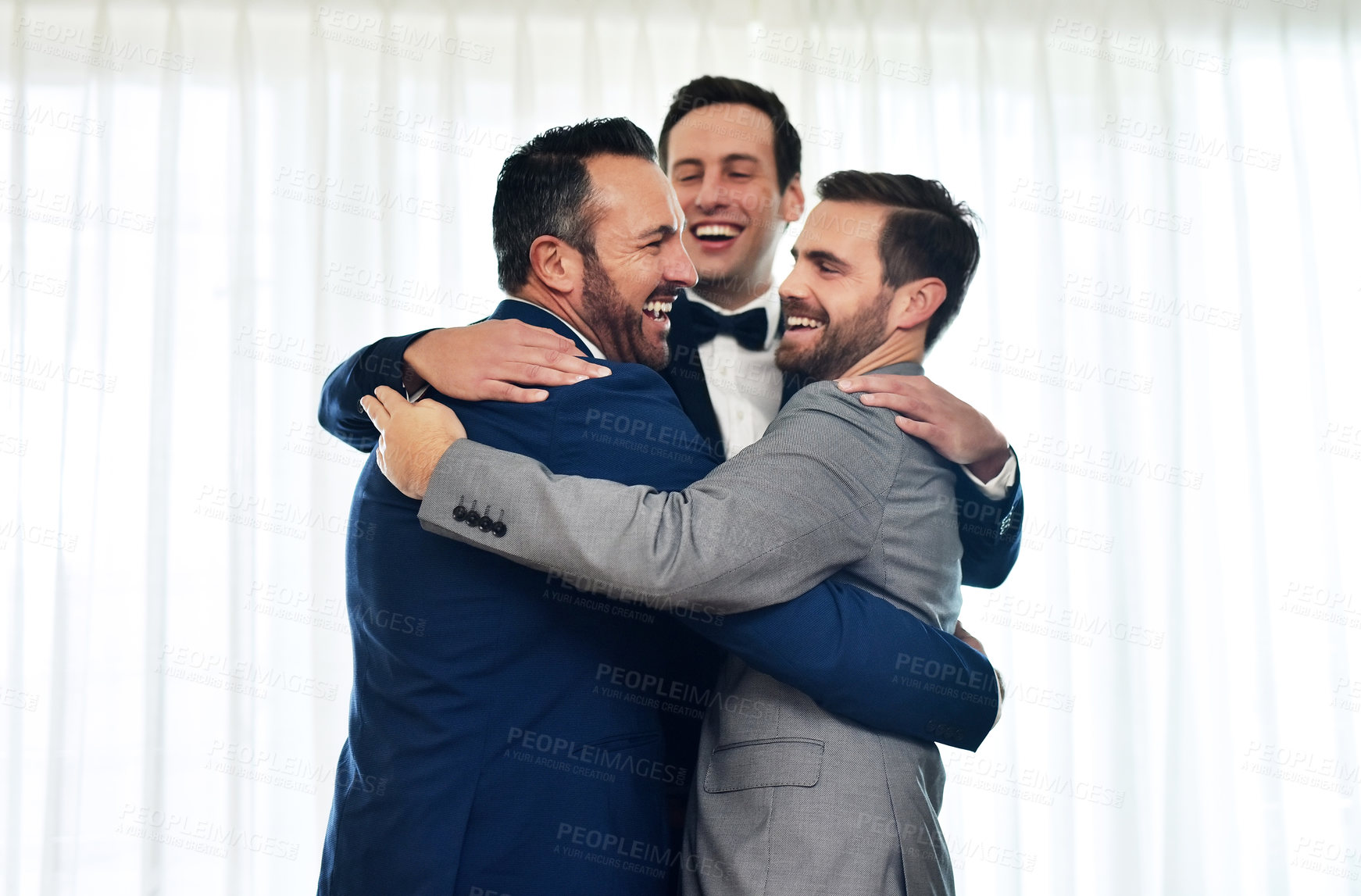 Buy stock photo Shot of two groomsmen hugging and celebrating with the bridegroom on his wedding way