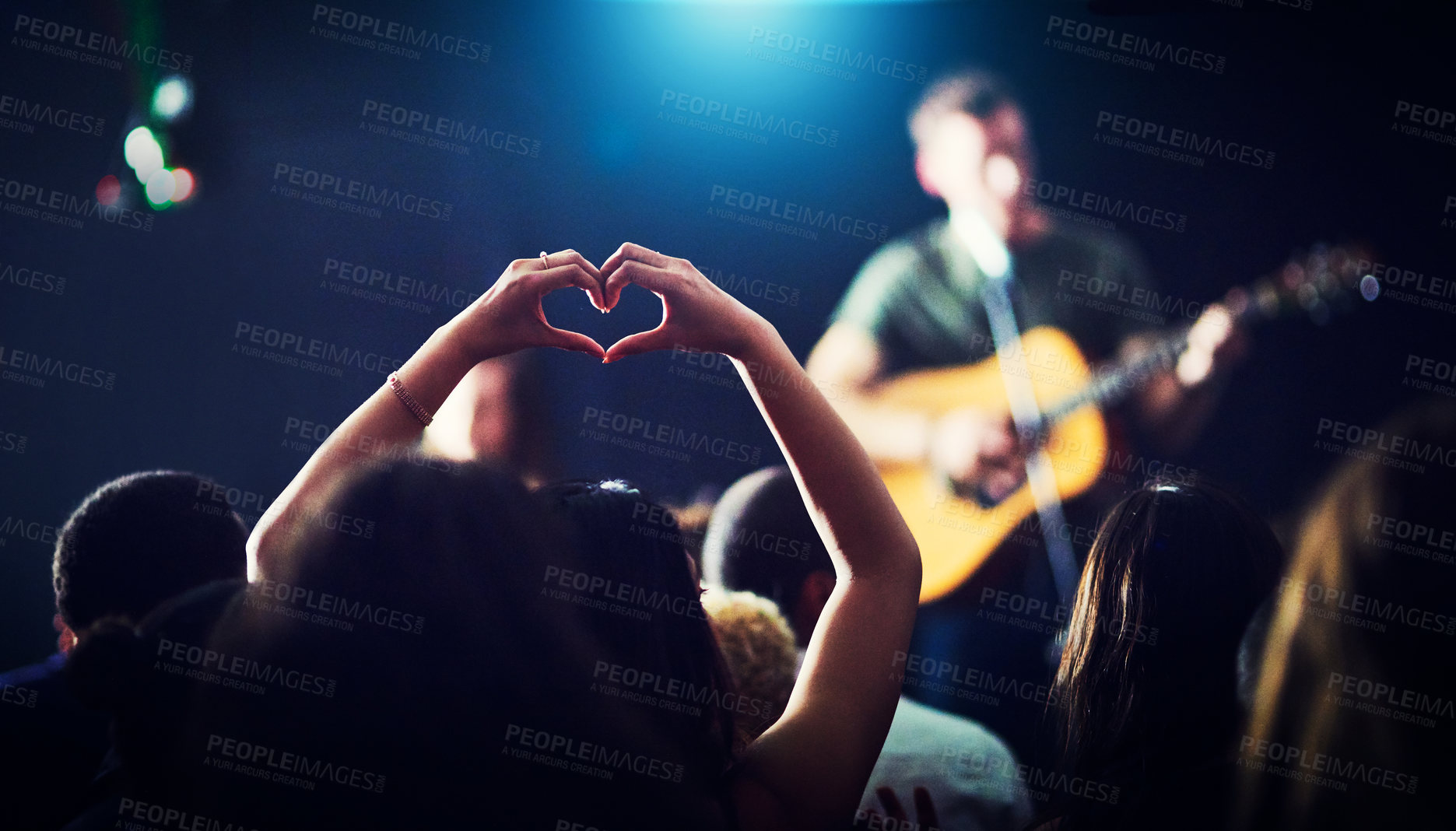 Buy stock photo Cropped shot of an unrecognizable woman's hands making a heart shape while a musician is performing at a concert at night