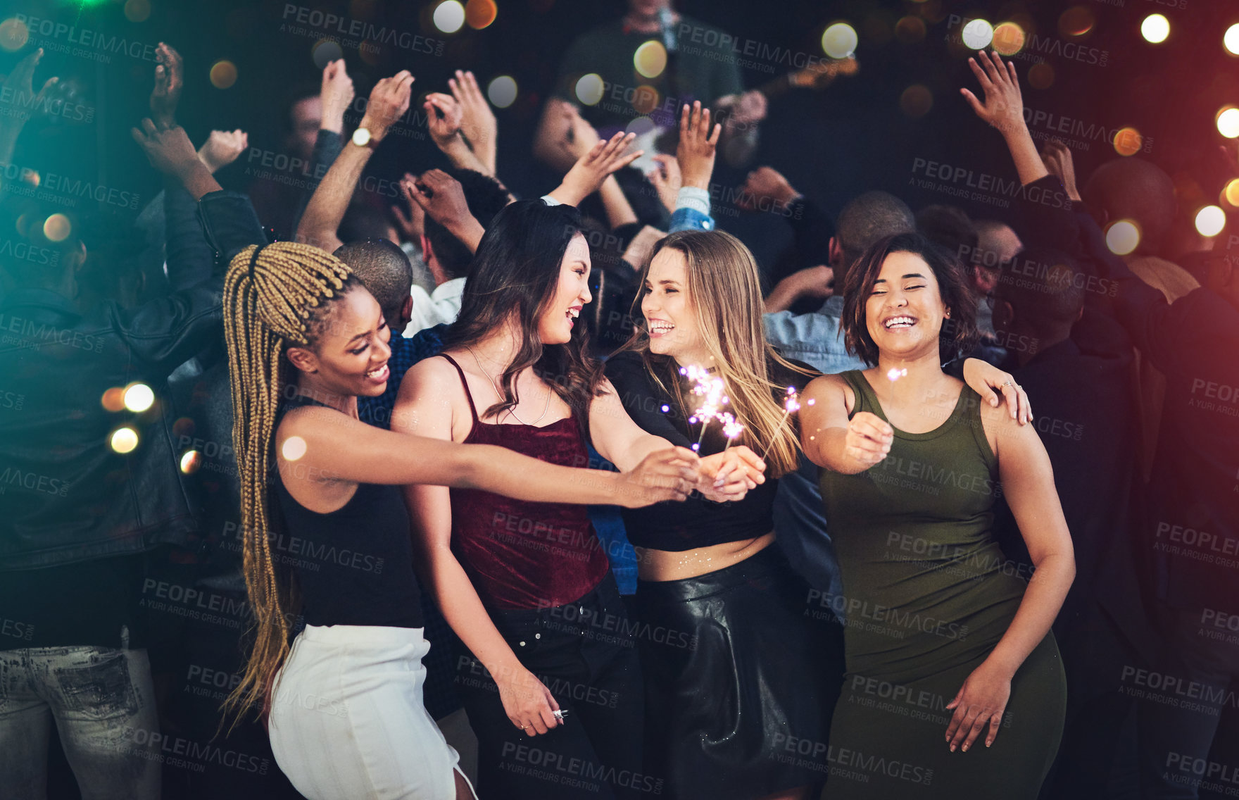Buy stock photo Cropped shot of a diverse group of young friends having fun with sparklers at a party at night