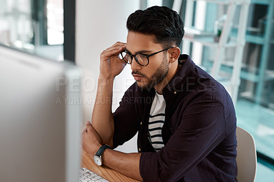 Buy stock photo Cropped shot of a handsome young businessman sitting alone and looking contemplative while using his computer in the office