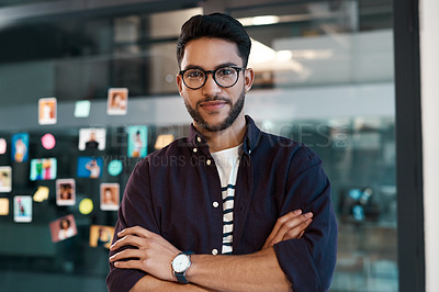 Buy stock photo Cropped portrait of a handsome young businessman wearing spectacles and standing alone in his office with his arms folded