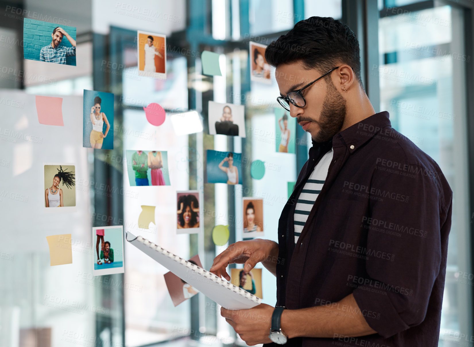 Buy stock photo Cropped shot of a handsome young businessman wearing spectacles and standing alone in his office while reading paperwork