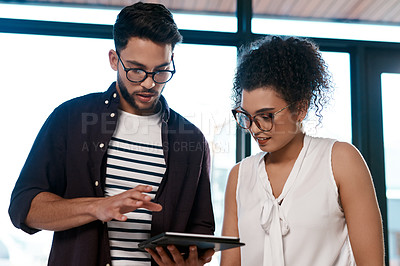 Buy stock photo Cropped shot of a two young business colleagues standing together in the office and working on a tablet