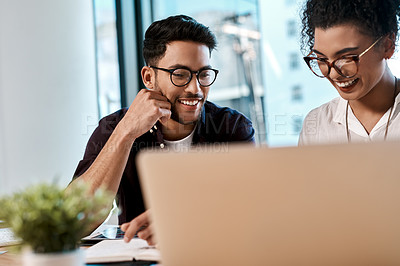 Buy stock photo Cropped shot of two young business colleagues sitting together and looking at a laptop in the office