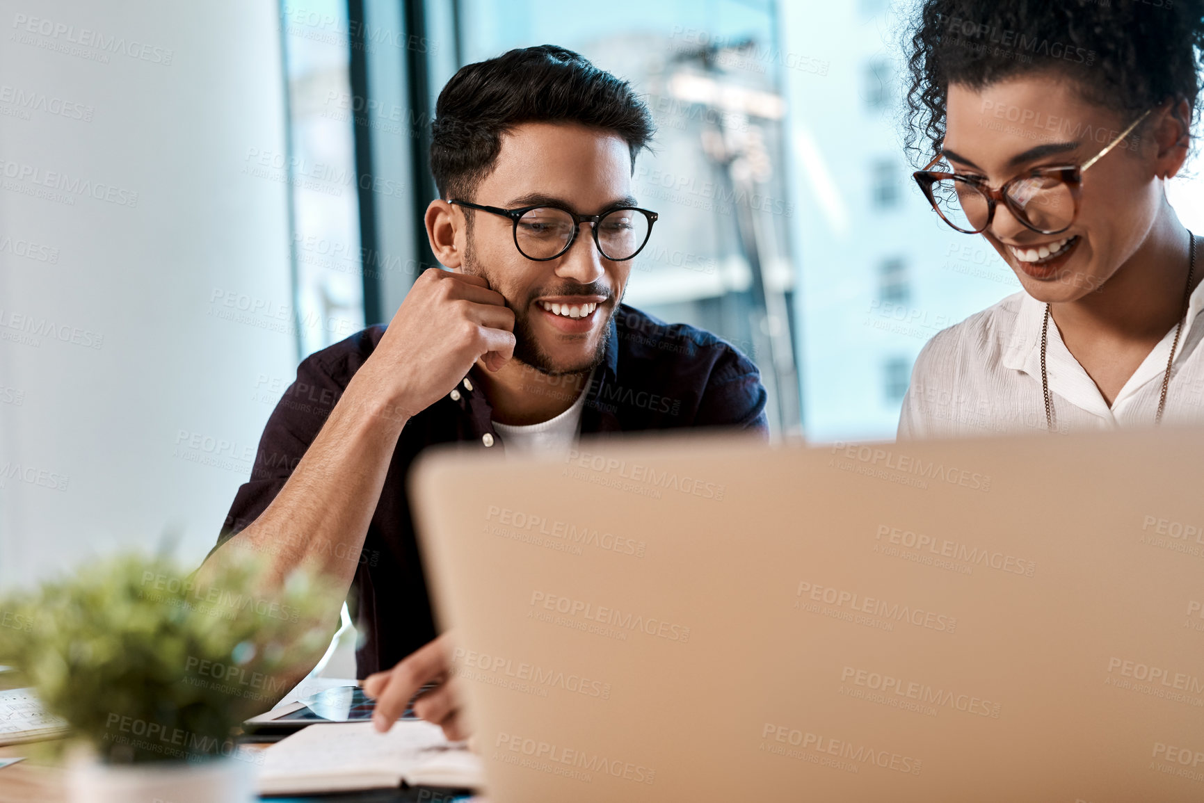 Buy stock photo Cropped shot of two young business colleagues sitting together and looking at a laptop in the office