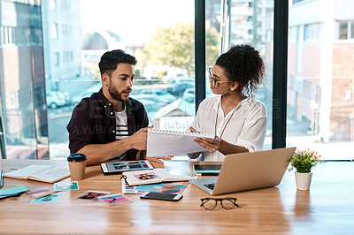 Buy stock photo Cropped shot of two young businesspeople siting together in the office and reading paperwork during a meeting