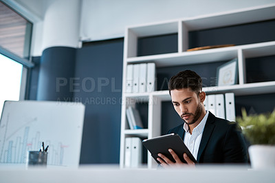 Buy stock photo Cropped shot of a handsome young businessman sitting alone and using a tablet in his office